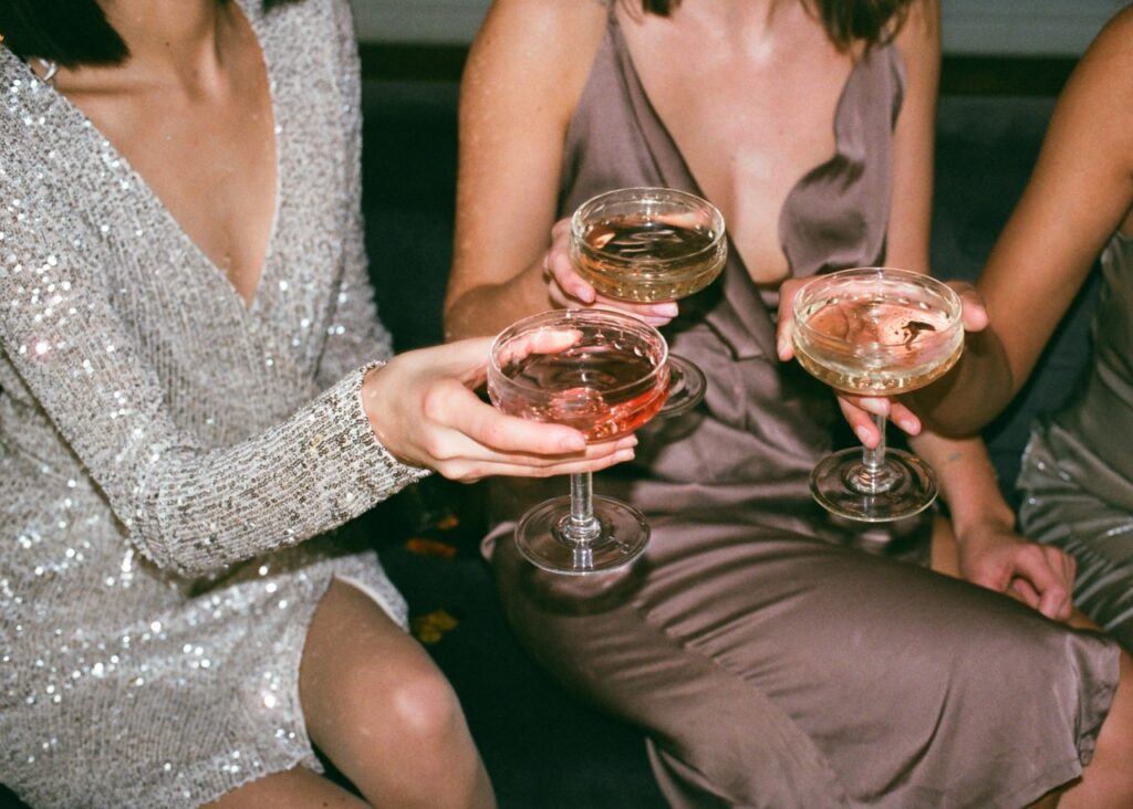 Three women sitting on a bench holding wine glasses.