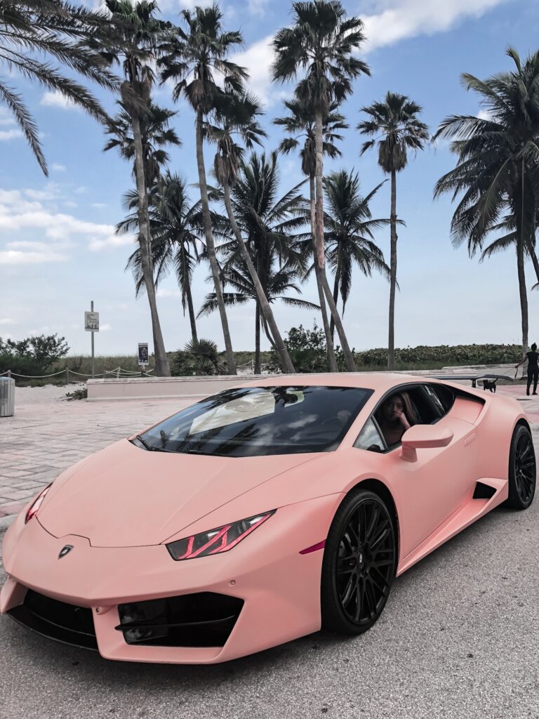 A pink car parked on the beach near palm trees.