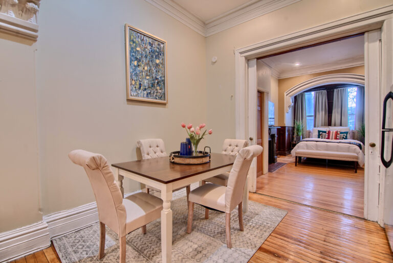 A dining room table with four chairs and a painting on the wall.