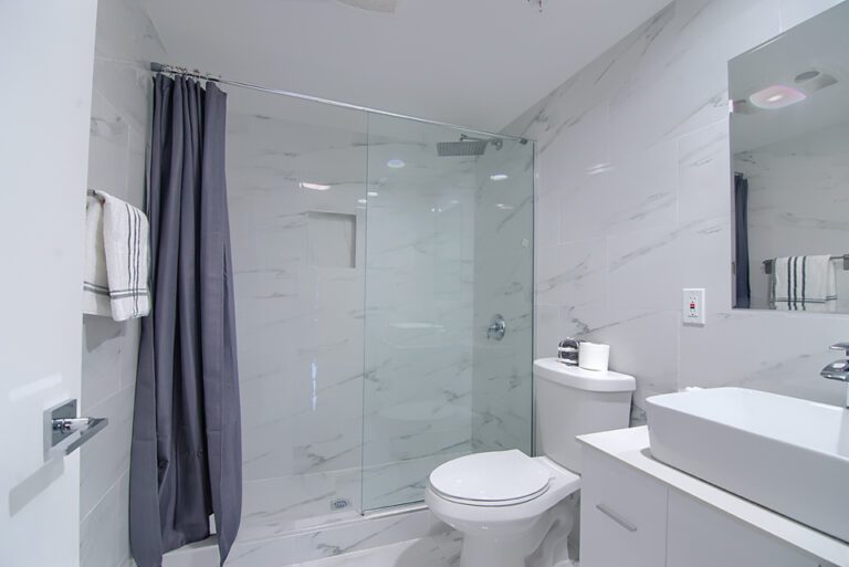 A bathroom with white tile and glass shower.