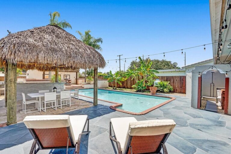 A pool with an umbrella and chairs in the back.