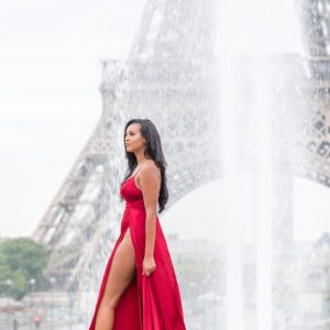 A woman in red dress standing next to the eiffel tower.