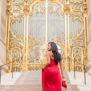 A woman in red dress standing on steps near gold door.